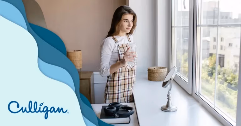 Femme qui regarde à la fenêtre avec un verre d'eau