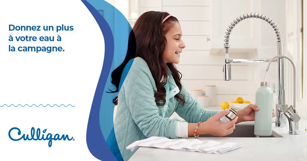 Petite fille souriante qui remplie une bouteille d'eau avec le robinet Culligan dans la cuisine