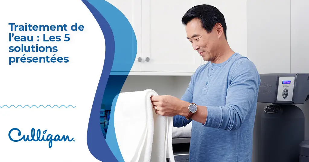 Un homme asiatique qui plie une serviette blanche dans la salle de lavage. Derrière lui on voit un appareil Culligan