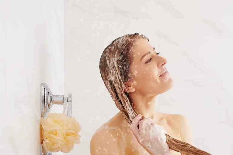 Une femme qui se lave les cheveux dans la douche en souriant