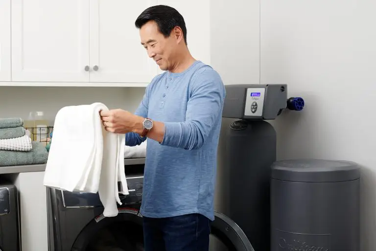 Un homme asiatique qui plie une serviette blanche dans la salle de lavage. Derrière lui on voit un appareil Culligan