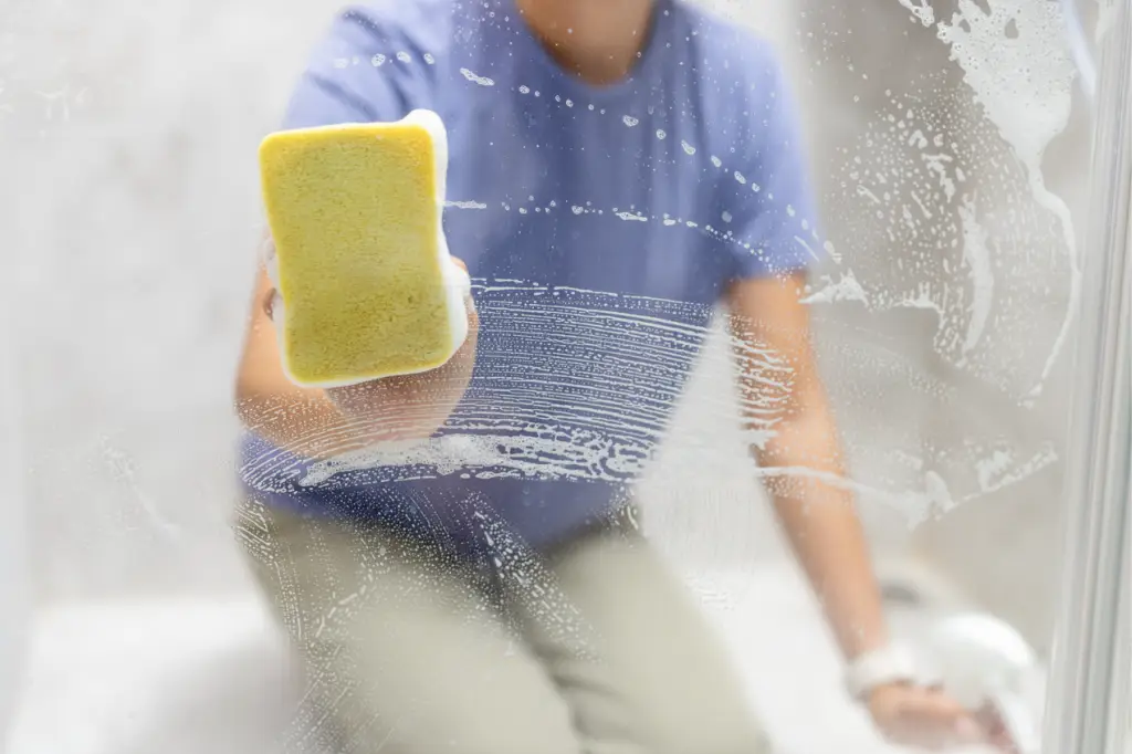 Femme qui lave une fenêtre avec une éponge jaune de l'eau et du savon