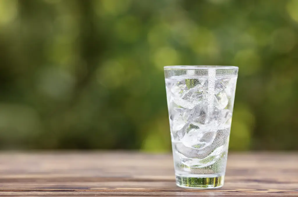 Une verre d'eau clair avec glace sur un fond flou estivale