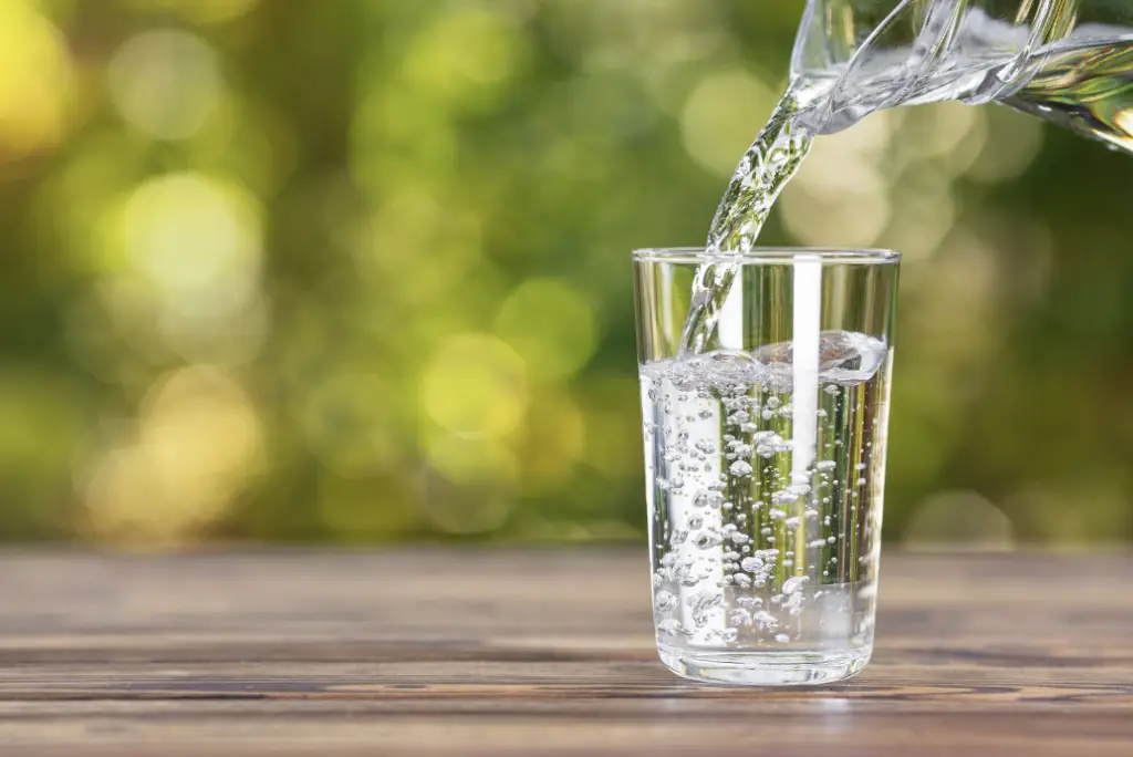Un pichet d'eau qui se dans un verre, l'eau est clair et limpide, l'arrière nous montre que c'est l'été