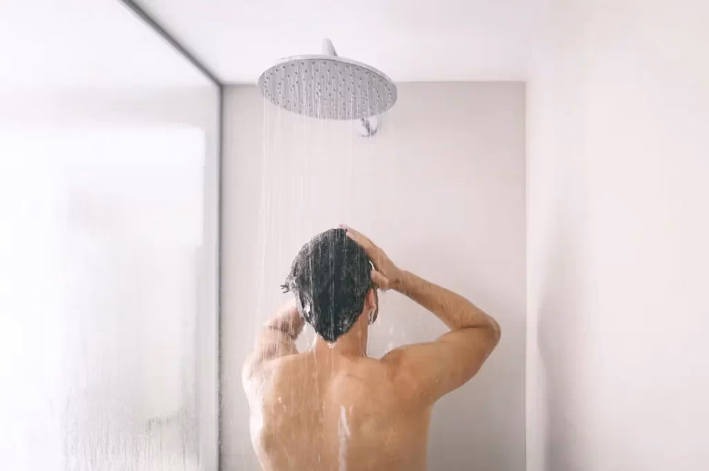 Homme vue de dos, qui se lave les cheveux dans une douche blanche