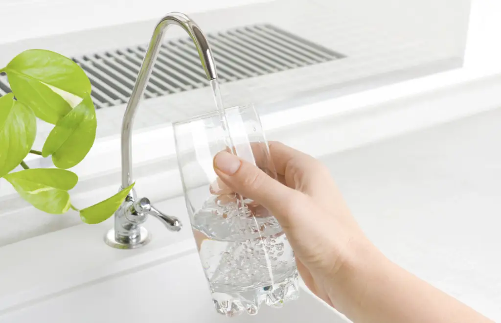 Vue rapprochée de la main d'une femme qui remplie un verre d'eau au robinet