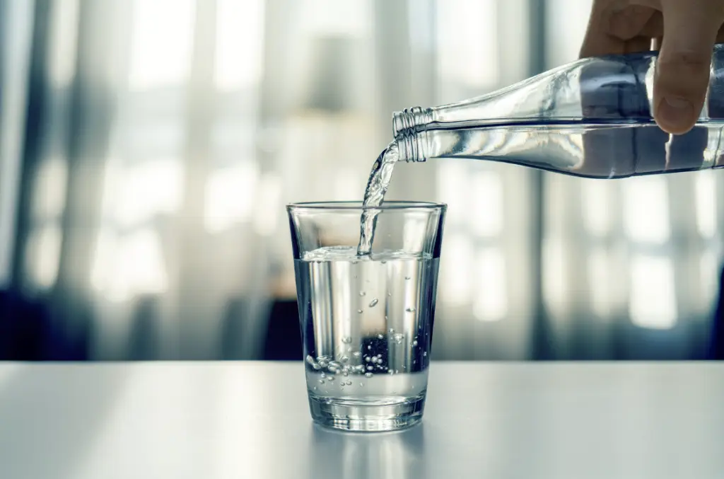 main versant une bouteille d'eau transparente dans un verre de vitre