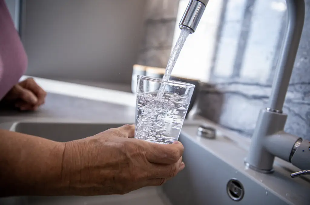 Une femme âgée qui remplie un verre d'eau avec le robinet de la cuisine