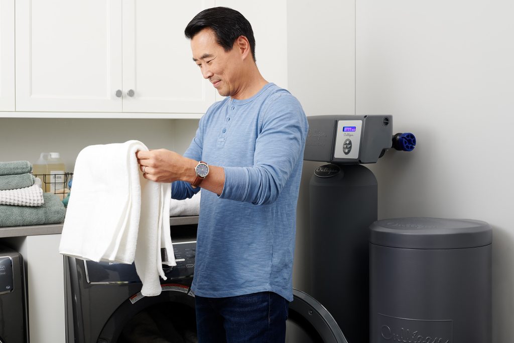 homme pliant serviette propre devant électroménager laveuse avec filtreurs adoucisseur à eau culligan
